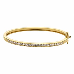 May include: A gold-toned oval bangle bracelet featuring a row of small, clear, round-cut stones set along the front half of the band. The bracelet includes a hinged side mechanism with a secure clasp closure, showcasing a polished metal finish.