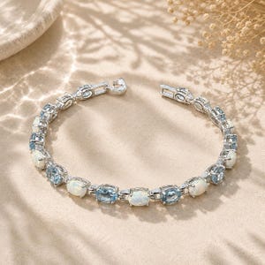 May include: A silver-toned link bracelet featuring alternating oval-shaped iridescent white opals and light blue faceted gemstones. The bracelet is constructed with individual metal settings for each stone and includes a secure clasp mechanism.