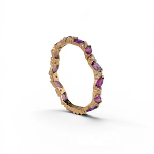 May include: A gold-colored ring with a continuous pattern of purple and white gemstones. The ring features marquise-cut purple stones and small, round white stones. The ring is set against a white background.