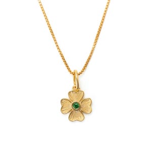 May include: Gold-colored necklace with a four-leaf clover pendant. The pendant has a green gemstone in the center. The chain is a delicate box chain style.