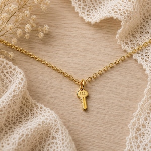 May include: A gold-toned necklace featuring a delicate chain and a small key-shaped pendant. The pendant is engraved with the number 111 on its head. The metal has a polished finish, and the design is simple, consisting of a thin link chain.