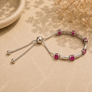 May include: A silver-toned adjustable bolo bracelet featuring a box chain, a sliding bead clasp, and five square-cut vibrant pink stones set in silver frames, alternating with smooth silver-toned cylindrical metal spacers along the chain.