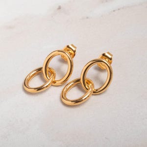May include: A pair of gold-toned earrings with a double circle design. The earrings are made of metal and have a polished finish.