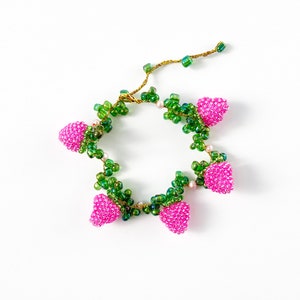 Könnte beinhalten: Ein rosa-grünes Perlenarmband mit Erdbeer-Design. Das Armband besteht aus kleinen Perlen und hat einen zarten, femininen Look.