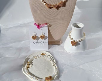 May include: A set of pearl jewelry with gold heart accents. The set includes a necklace, bracelet, and earrings. The jewelry is displayed on a white background.