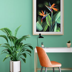 Puede incluir: Una impresi&oacute;n enmarcada de una pintura que representa dos flores de ave del para&iacute;so naranja, azul y verde sobre un fondo oscuro. La impresi&oacute;n est&aacute; colgada en una pared verde claro sobre un escritorio blanco con una silla de cuero marr&oacute;n.