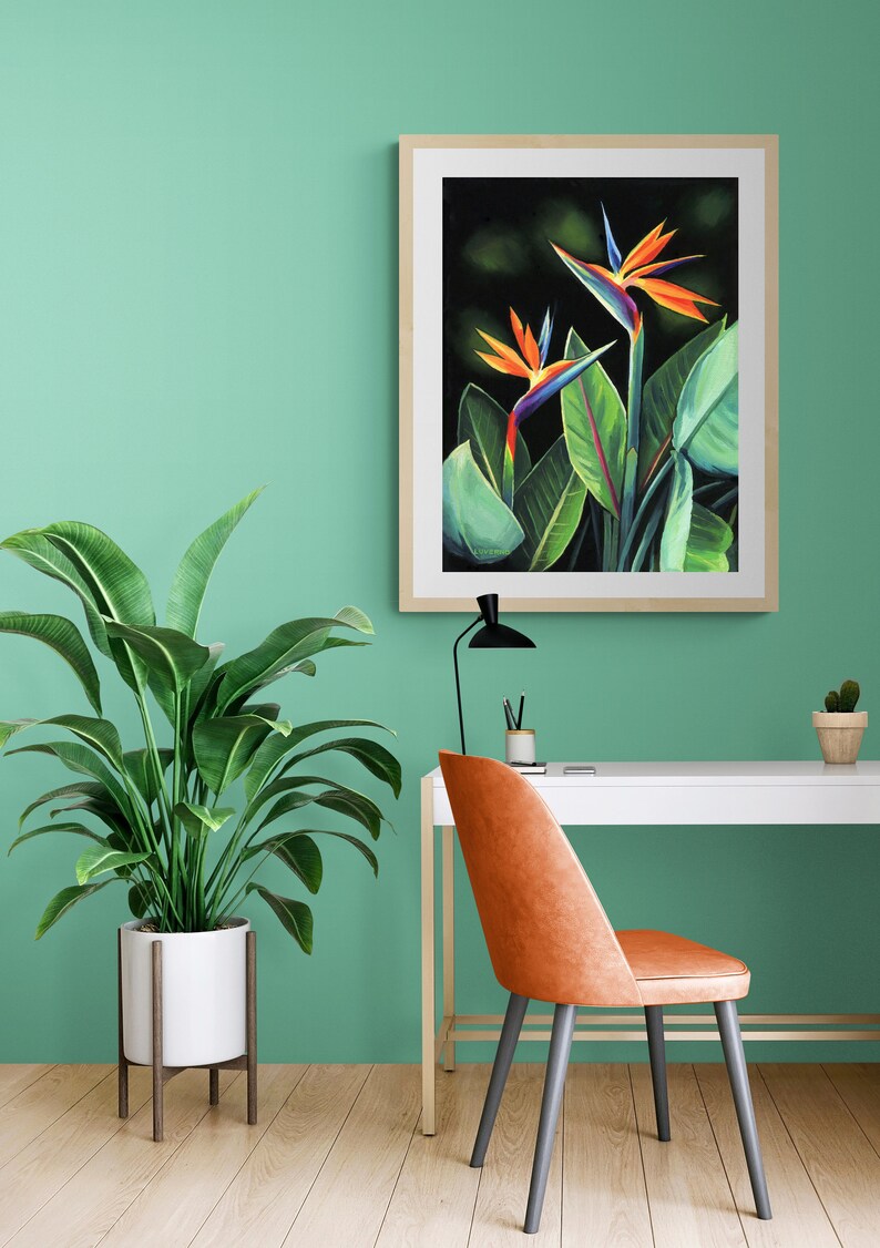 Puede incluir: Una impresi&oacute;n enmarcada de una pintura que representa dos flores de ave del para&iacute;so naranja, azul y verde sobre un fondo oscuro. La impresi&oacute;n est&aacute; colgada en una pared verde claro sobre un escritorio blanco con una silla de cuero marr&oacute;n.