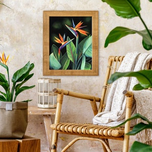 Puede incluir: Una impresi&oacute;n enmarcada de una flor de ave del para&iacute;so con colores naranja, azul y verde. La impresi&oacute;n est&aacute; colgada en una pared con una silla de mimbre y plantas en macetas en primer plano.