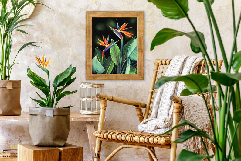 Puede incluir: Una impresi&oacute;n enmarcada de una flor de ave del para&iacute;so con colores naranja, azul y verde. La impresi&oacute;n est&aacute; colgada en una pared con una silla de mimbre y plantas en macetas en primer plano.