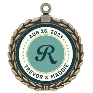 May include: A round, bronze-colored medal with a laurel wreath border. The center features a teal circle with the letter "R" and the text "AUG 26, 2023" and "TREVOR & MADDIE".
