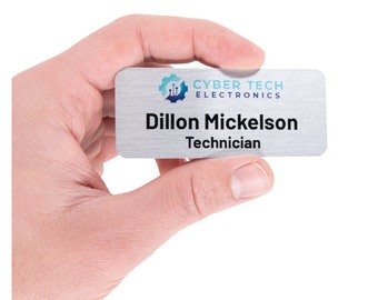 Może przedstawiać: Srebrna tabliczka z nazwiskiem z niebiesko-białym logo, na którym widnieje napis "Cyber Tech Electronics". Na tabliczce widnieje napis "Dillon Mickelson Technik".