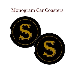 May include: Two black round car coasters with a cut-out for a cup. Each coaster features a gold letter "S" in a decorative font.