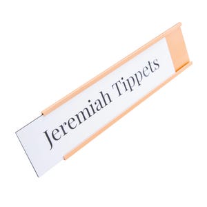 May include: A peach-coloured nameplate with the name "Jeremiah Tippets" printed in black on a white background. The nameplate is angled, and the text is centred.