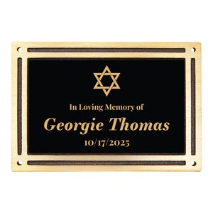 May include: A rectangular bronze memorial plaque with a black center. The plaque features the Star of David, the text "In Loving Memory of Georgie Thomas 10/17/2025", and a decorative border with mounting holes.