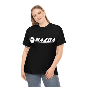 Könnte beinhalten: Schwarzes T-Shirt mit weißem Mazda-Logo. Das Logo zeigt ein stilisiertes 'M' in einem Kreis, gefolgt vom Markennamen in einer klaren, serifenlosen Schrift. Das T-Shirt hat einen klassischen Rundhalsausschnitt.
