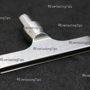 May include: A silver metal T-shaped tool with a rounded handle and a flat, rectangular blade.