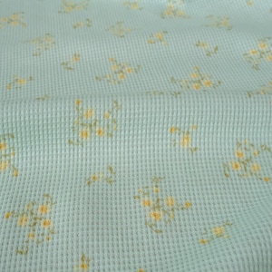 May include: A light blue waffle weave fabric with a small floral pattern in yellow. The fabric is soft and textured.