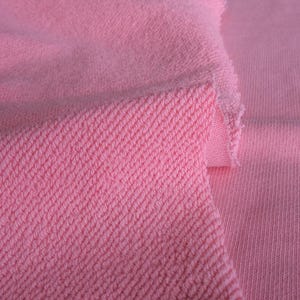 K&ouml;nnte beinhalten: Nahaufnahme von rosa Stoff mit diagonal gewebter Textur links und glatter Rippenstruktur rechts. Der Stoff wirkt weich und eignet sich m&ouml;glicherweise f&uuml;r Kleidung oder Textilprojekte.