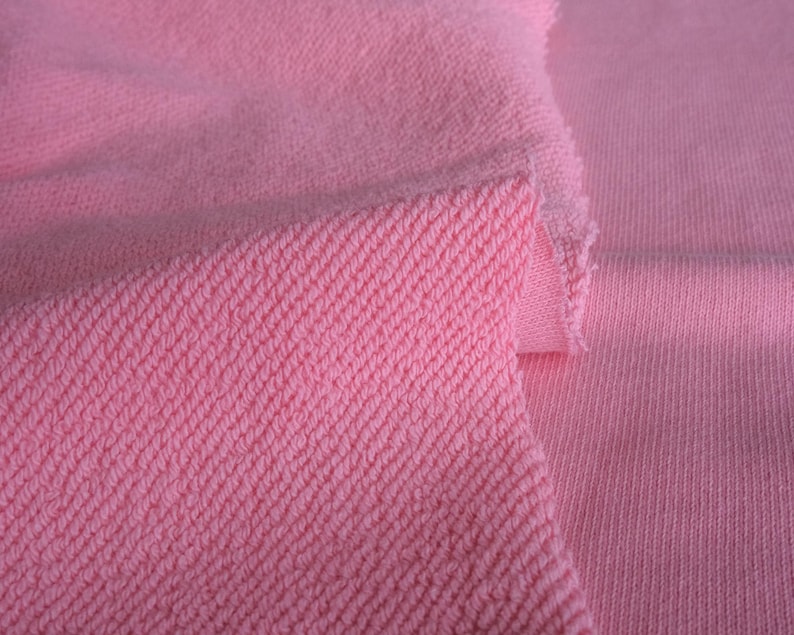 K&ouml;nnte beinhalten: Nahaufnahme von rosa Stoff mit diagonal gewebter Textur links und glatter Rippenstruktur rechts. Der Stoff wirkt weich und eignet sich m&ouml;glicherweise f&uuml;r Kleidung oder Textilprojekte.
