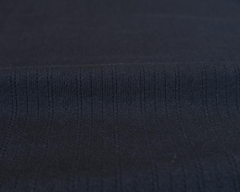 May include: Close-up of a dark blue fabric with a textured, ribbed pattern. The fabric has a smooth, soft feel.