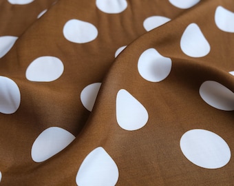 May include: Close-up of a brown fabric with large white polka dots. The fabric is draped, creating soft folds and shadows. The polka dots vary slightly in shape, adding visual interest to the textile.