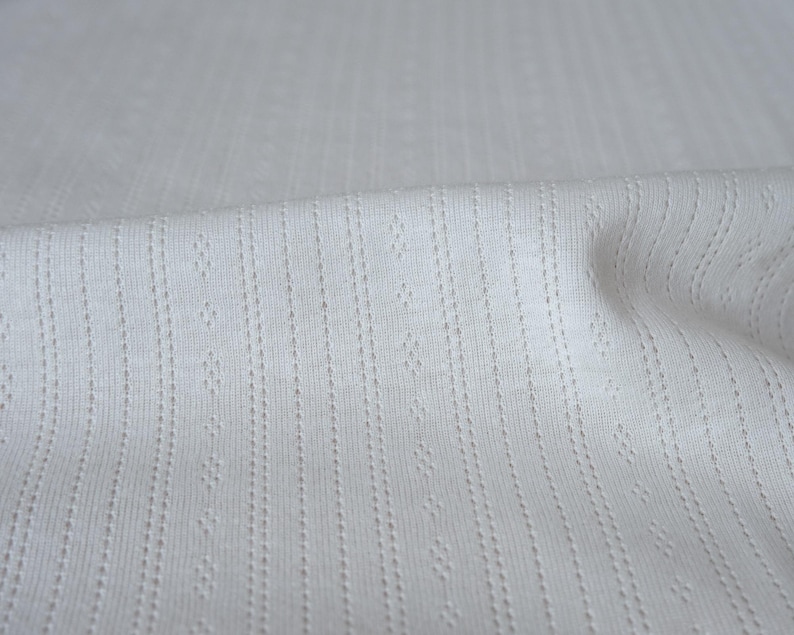 May include: White fabric with a textured, ribbed pattern. The fabric has a subtle sheen and a soft, smooth feel.