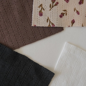 May include: Four fabric swatches in different colors and patterns. The swatches are brown, black, white, and a floral pattern with pink flowers on a cream background.