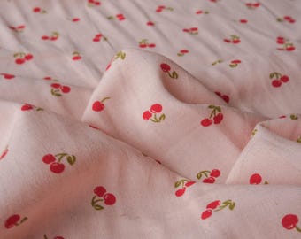 May include: Pink fabric with a repeating pattern of red cherries. The fabric is folded and has a soft, textured appearance.