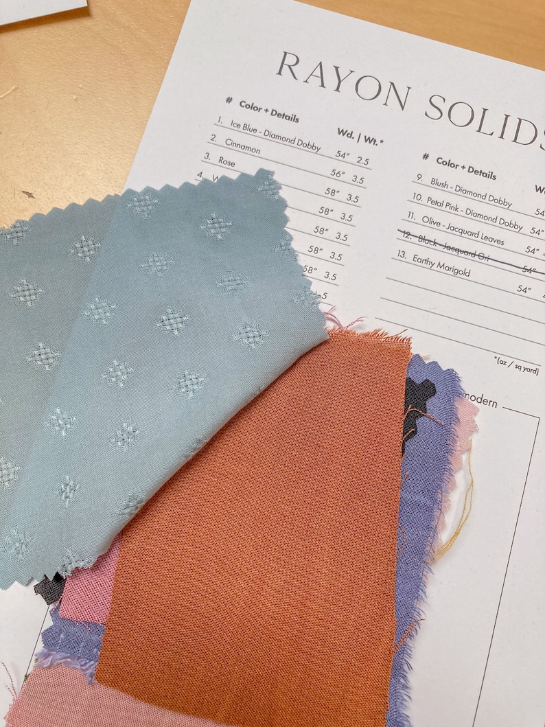 May include: A close-up of fabric swatches in various colors, including light blue, pink, and orange. The swatches are arranged on a white sheet of paper with a list of fabric details and measurements in inches.