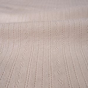 May include: Close-up of a beige ribbed fabric with a subtle textured pattern. The fabric has a soft, smooth feel and is perfect for creating garments or home decor projects.