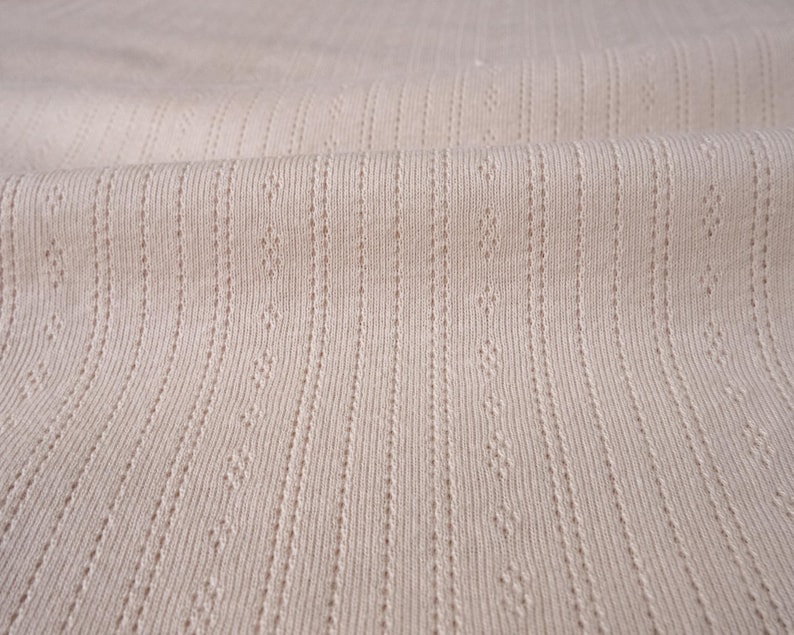May include: Close-up of a beige ribbed fabric with a subtle textured pattern. The fabric has a soft, smooth feel and is perfect for creating garments or home decor projects.