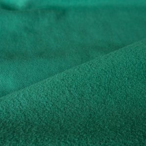 Pode incluir: Close-up de um tecido verde esmeralda texturizado. O tecido tem uma textura macia e ligeiramente difusa de um lado e uma textura canelada do outro. O tecido est&aacute; dobrado, criando sombras e profundidade.