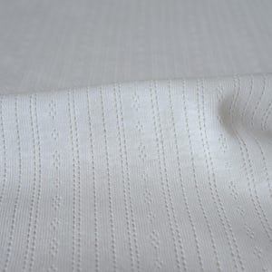 May include: White fabric with a textured, ribbed pattern. The fabric has a subtle sheen and a soft, smooth feel.