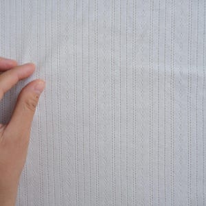 May include: Close-up of a white fabric with a textured pattern of vertical lines and small dots.