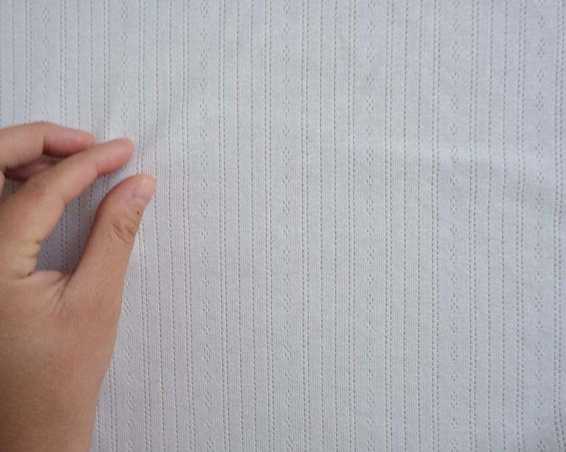 May include: Close-up of a white fabric with a textured pattern of vertical lines and small dots.