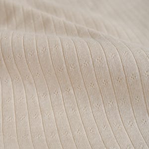 May include: Close-up of a beige ribbed fabric with a subtle textured pattern.