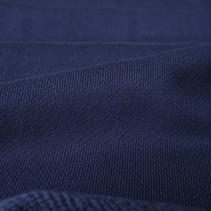 Puede incluir: Primer plano de una tela de punto acanalado azul marino. La tela tiene una superficie texturizada con l&iacute;neas verticales y pliegues sutiles, creando una sensaci&oacute;n de profundidad. El color es un azul profundo y saturado.