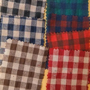 May include: A collection of fabric swatches in various colors, each featuring a classic gingham pattern. The swatches include black and tan, navy blue, brown, green, red, and white. The edges of the fabric are unfinished.