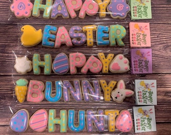 May include: A set of five decorated sugar cookies spelling out "Happy Easter Bunny Hunt". Each cookie is decorated with different pastel colors and patterns.