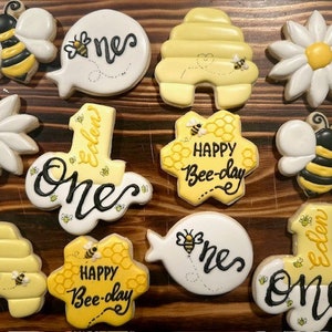 May include: A set of 10 decorated sugar cookies featuring a bee theme. The cookies are decorated with yellow, white, and black icing. Some cookies have the words "Happy Bee-day" and "One" written on them. Other cookies feature a bee, a honeycomb, and a daisy.