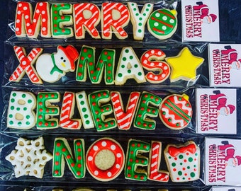May include: A set of six Christmas cookie cutters, each with a different holiday word or design. The cutters are arranged in a row, with the words "Joyful", "Merry", "Xmas", "Believe", "Noel", and "Jolly" visible. Each cutter is decorated with red, green, and white icing.