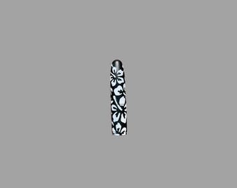 May include: A cylindrical lipstick tube featuring a matte black base color with a repeating white floral pattern covering the entire exterior surface. The design consists of stylized hibiscus-like flowers and leaves arranged in a continuous print.
