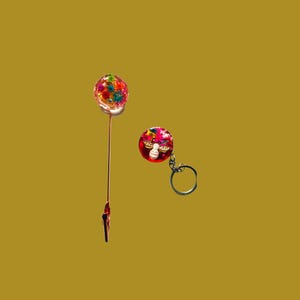 May include: A colorful, round resin paper clip and keychain set. The paper clip has a long, thin stem and a clip at the bottom. The keychain has a silver ring. Both items have a vibrant, multi-colored design.