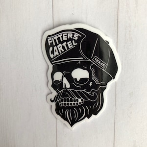 May include: Black and white sticker featuring a skull with a mustache and beard, wearing a cap with the words "FITTERS CARTEL" and "TEXAS". The sticker has a glossy finish and is set against a white background.