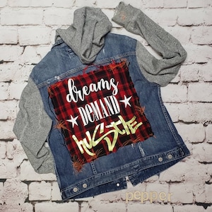May include: A blue denim jacket with a gray hooded sweatshirt attached to the sleeves. The back of the jacket has a red and black plaid patch with the text "dreams demand hustle" in gold lettering.