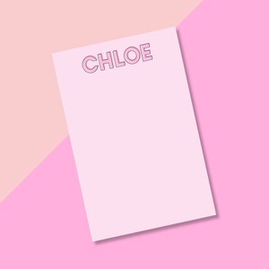 May include: A pink notepad with the name "CHLOE" written in a pink outlined font on a pink and peach background.
