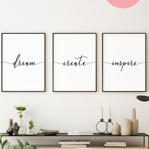Peut inclure: Trois impressions encadrées noires avec des fonds blancs et une calligraphie noire. Les impressions indiquent "dream", "create" et "inspire". Les impressions sont accrochées à un mur blanc au-dessus d'une console en bois avec deux tiroirs.