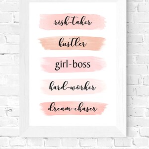 May include: A white framed print with pink watercolor brushstrokes and the words "risk-taker", "hustler", "girl-boss", "hard-worker", and "dream-chaser" in black cursive font.