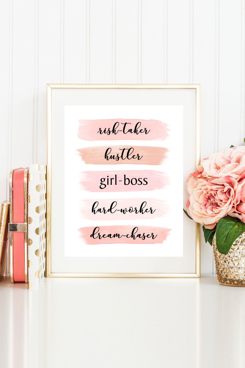 May include: A framed print with a white background and pink watercolor brushstrokes. The text on the print reads "risk-taker, hustler, girl-boss, hard-worker, dream-chaser".
