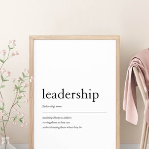 May include: A framed print with the word "leadership" in a bold, black font. The definition of the word is written in a smaller font below, "[lēder-ship] noun inspiring others to achieve serving them so they can and celebrating them when they do."